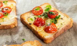 Pyszna, lekka kolacja: tosty z roztopionym serem, pieczonymi pomidorkami koktajlowymi i szczypiorkiem.