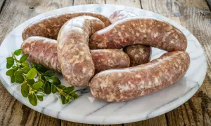 Surowa biała kiełbasa na marmurowej desce, z gałązką zieleni. Dowiedz się, ile czasu gotować białą kiełbasę, by była idealna.