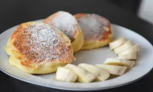 Szybkie placuszki na śniadanie, posypane cukrem pudrem, podane z plasterkami banana na białym talerzu.