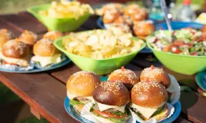 Mini burgery z serem i sałatą, miski chipsów i sałatki na piknikowym stole. Idealna szybka przekąska na letnie popołudnie.