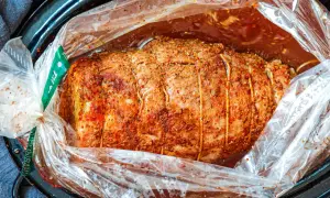 Soczysta szynka pieczona w rękawie, przyprawiona i związana sznurkiem, gotowa do pieczenia w aromatycznym sosie.