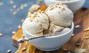 Trzy gałki lodów z mascarpone, posypane kruszonką i ziarnami słonecznika, w białej miseczce na drewnianej desce.