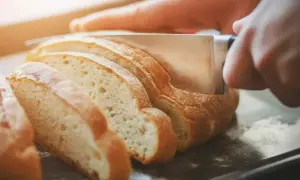 Ręka kroi świeży chleb, pokazując, jak odświeżyć pieczywo.