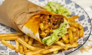 Pyszny kebab w tortilli z chrupiącymi frytkami i świeżą sałatką na talerzu.