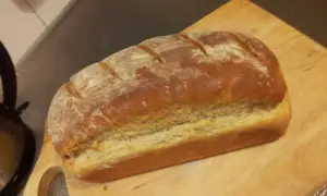 Pyszny, świeżo upieczony przaśny chleb z chrupiącą skórką, posypany mąką, leży na drewnianej desce.