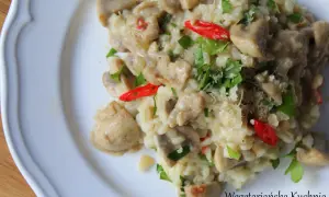 Kremowe risotto z pieczarkami, ozdobione natką pietruszki i kawałkami papryczki chili. Idealne danie dla miłośników wegetariańskiej kuchni.