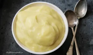 Gładki, żółty krem patissiere w białej miseczce, obok dwie łyżeczki. Idealny do deserów.