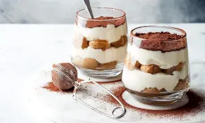 Dwa pucharki z kremowym tiramisu, posypane kakao. Idealna mizeria na słodko, która rozpływa się w ustach.