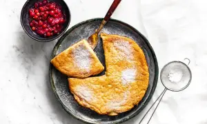 Puszysty omlet z air fryera, posypany cukrem pudrem, z łyżką żurawiny i sitkiem do cukru.