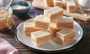 Słodkie wafle przełożone kremową masą do wafli, ułożone na talerzu. Obok słoik z masą i miseczka z wiórkami.