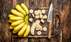 Pęczek żółtych bananów, pokrojonych w plasterki i obok nóż na desce. Zastanawiasz się, czy banany można trzymać w lodówce?