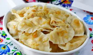 Pyszne pierogi ukraińskie z cebulką i skwarkami, podane w białej misce na kolorowym obrusie.
