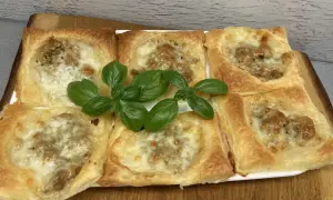 Sześć kwadratowych porcji ciasta francuskiego z mięsem mielonym i serem, ozdobione świeżą bazylią.