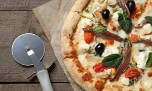 Pyszna pizza margarita z anchois, oliwkami i pomidorkami koktajlowymi, gotowa do pokrojenia.