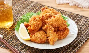 Chrupiące, złociste karaage na talerzu z sałatą i cytryną, obok szklanka piwa i pałeczki.