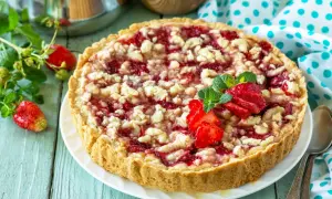 Pyszna tarta z truskawkami i kruszonką, ozdobiona świeżymi owocami i miętą, kusi apetycznym wyglądem.