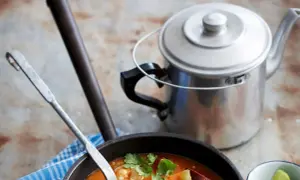Gęste, aromatyczne gumbo z krewetkami i kiełbasą, gotowe do podania. Obok metalowy czajniczek i ćwiartki limonki.