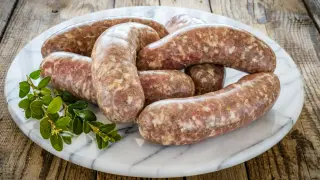 Surowa biała kiełbasa na marmurowej desce, z gałązką zieleni. Dowiedz się, ile czasu gotować białą kiełbasę, by była idealna.