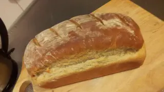 Pyszny, świeżo upieczony przaśny chleb z chrupiącą skórką, posypany mąką, leży na drewnianej desce.