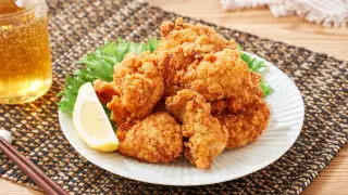 Chrupiące, złociste karaage na talerzu z sałatą i cytryną, obok szklanka piwa i pałeczki.