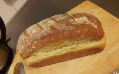Pyszny, świeżo upieczony przaśny chleb z chrupiącą skórką, posypany mąką, leży na drewnianej desce.