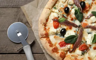 Pyszna pizza margarita z anchois, oliwkami i pomidorkami koktajlowymi, gotowa do pokrojenia.