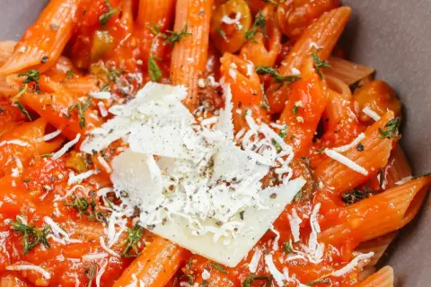 Szybki obiad z makaronem penne w sosie pomidorowym, posypany parmezanem i ziołami. Idealny na szybki posiłek.
