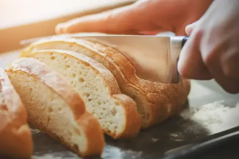Ręka kroi świeży chleb, pokazując, jak odświeżyć pieczywo.