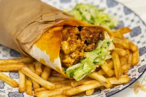 Pyszny kebab w tortilli z chrupiącymi frytkami i świeżą sałatką na talerzu.