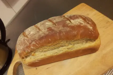 Pyszny, świeżo upieczony przaśny chleb z chrupiącą skórką, posypany mąką, leży na drewnianej desce.