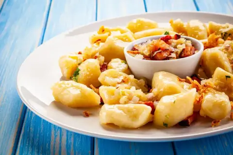 Pyszny obiad z jajek: leniwe pierogi z boczkiem i cebulką na białym talerzu, na niebieskim, drewnianym tle.