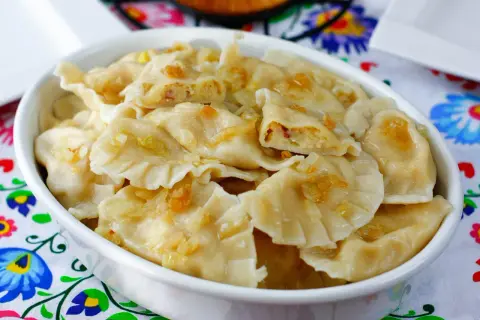 Pyszne pierogi ukraińskie z cebulką i skwarkami, podane w białej misce na kolorowym obrusie.