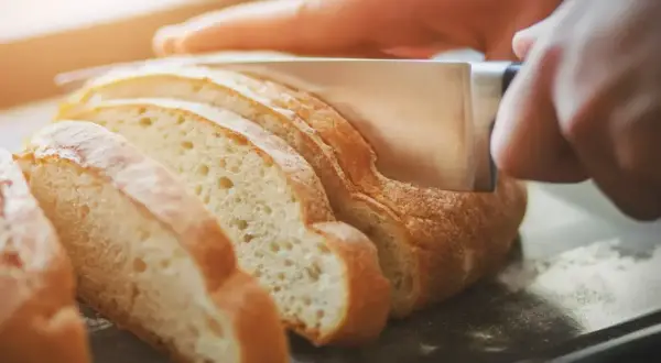 Ręka kroi świeży chleb, pokazując, jak odświeżyć pieczywo.