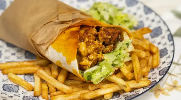 Pyszny kebab w tortilli z chrupiącymi frytkami i świeżą sałatką na talerzu.