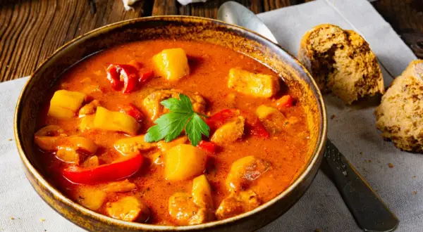 Aksamitna zupa gulaszowa przepis babci, pełna mięsa, ziemniaków i papryki, podana z chlebem.
