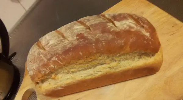Pyszny, świeżo upieczony przaśny chleb z chrupiącą skórką, posypany mąką, leży na drewnianej desce.
