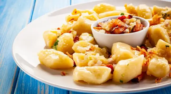 Pyszny obiad z jajek: leniwe pierogi z boczkiem i cebulką na białym talerzu, na niebieskim, drewnianym tle.