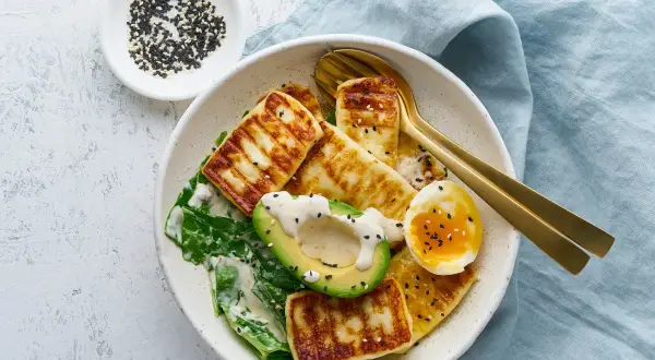 Szybki obiad keto: grillowany ser halloumi, awokado, jajko na miękko i zielone liście, posypane czarnym sezamem.