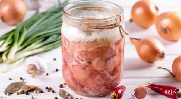 Słoik z domową kiełbasą w galarecie, obok cebula, czosnek, pieprz i chili. Idealny przepis na to, jak zrobić kiełbasę w słoiku z galaretką.