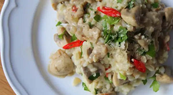 Kremowe risotto z pieczarkami, ozdobione natką pietruszki i kawałkami papryczki chili. Idealne danie dla miłośników wegetariańskiej kuchni.