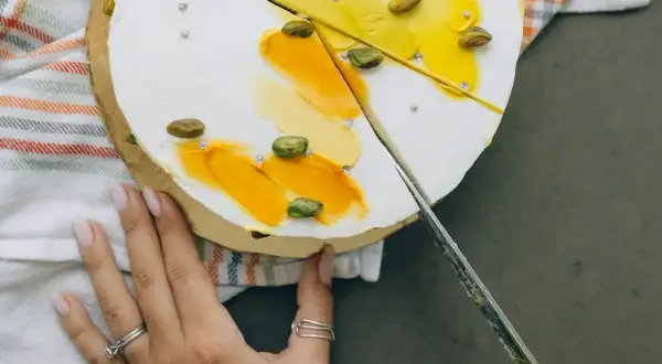 Delikatny tort z pistacjami i żółtym kremem, pokazujący, jak kroić tort, by zachować jego piękno.