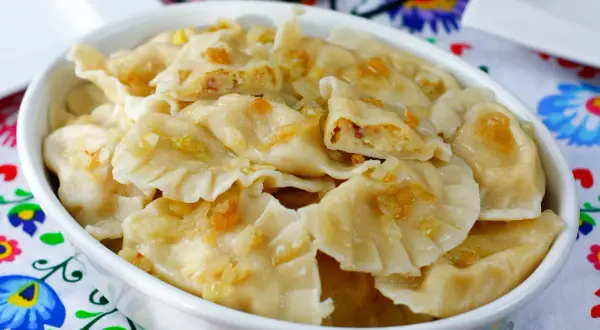 Pyszne pierogi ukraińskie z cebulką i skwarkami, podane w białej misce na kolorowym obrusie.