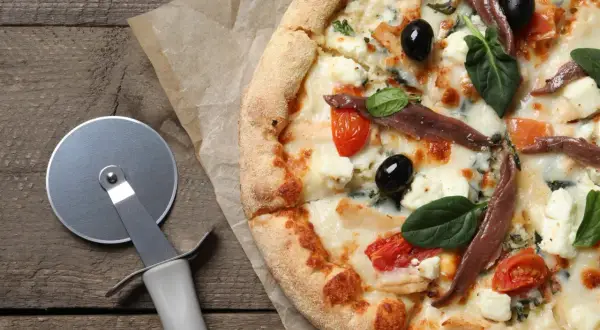 Pyszna pizza margarita z anchois, oliwkami i pomidorkami koktajlowymi, gotowa do pokrojenia.