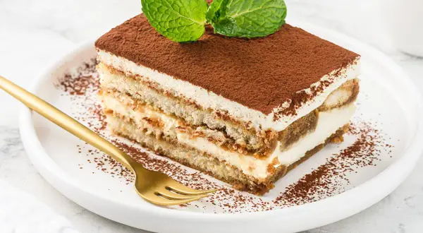 Pyszny kawałek tiramisu z mascarpone, posypany kakao i udekorowany miętą. Idealny na deser, gdy szukasz sprawdzonego przepisu.
