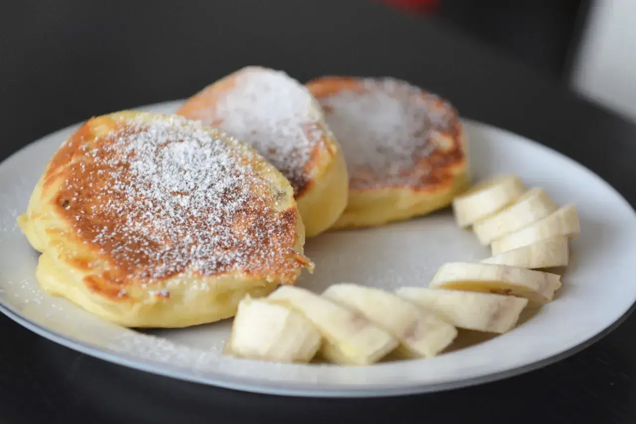 Szybkie placuszki na śniadanie, posypane cukrem pudrem, podane z plasterkami banana na białym talerzu.