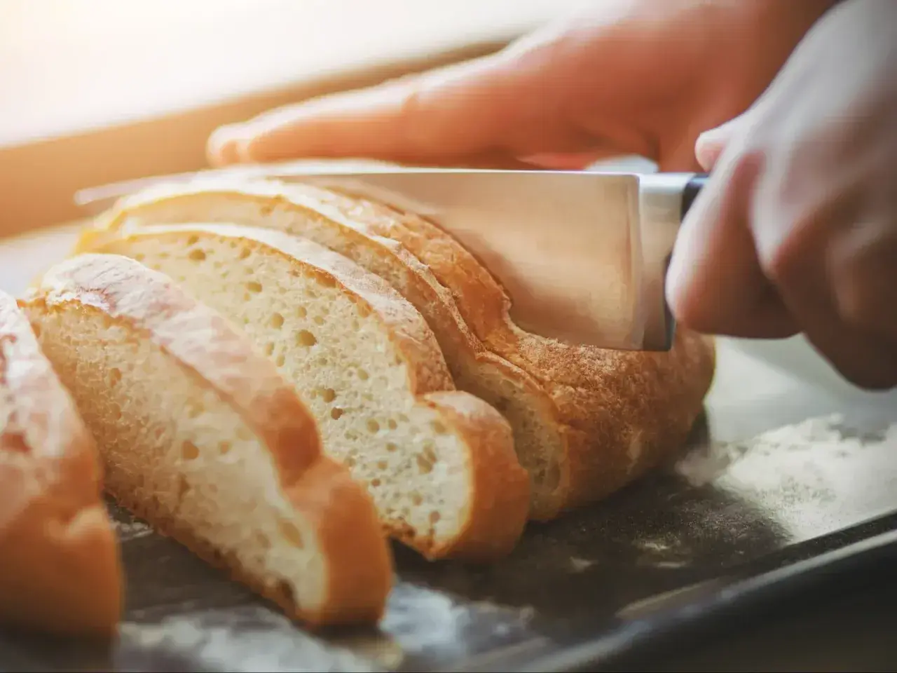 Ręka kroi świeży chleb, pokazując, jak odświeżyć pieczywo.