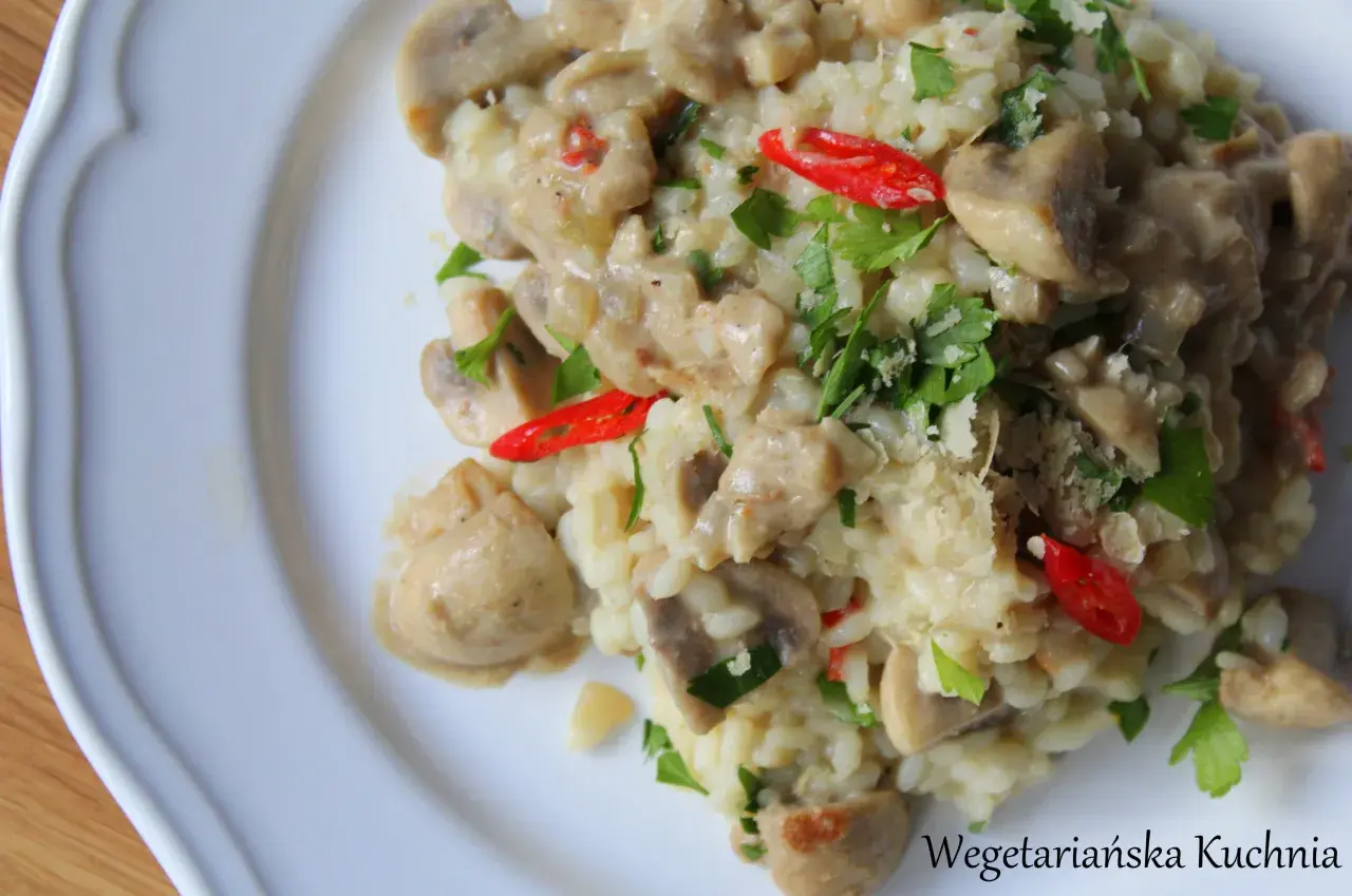 Kremowe risotto z pieczarkami, ozdobione natką pietruszki i kawałkami papryczki chili. Idealne danie dla miłośników wegetariańskiej kuchni.