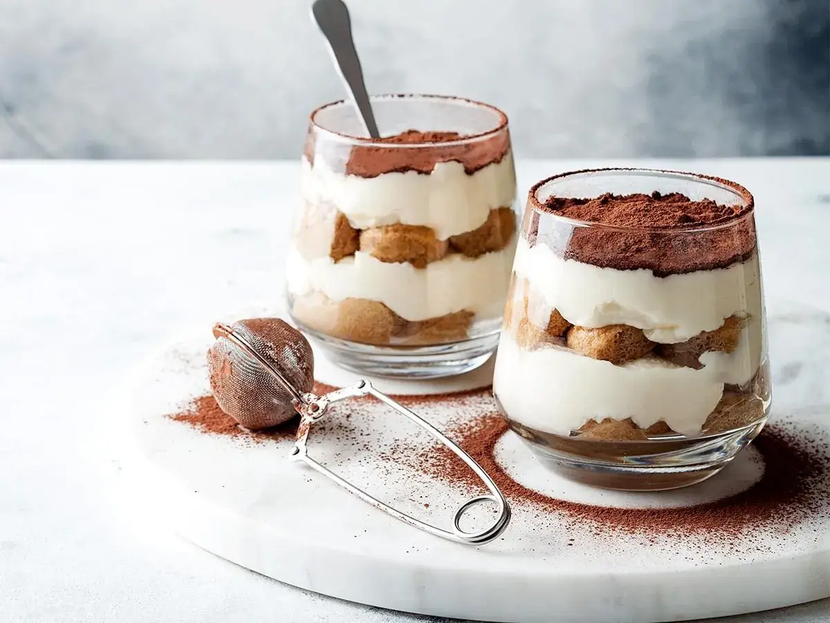 Dwa pucharki z kremowym tiramisu, posypane kakao. Idealna mizeria na słodko, która rozpływa się w ustach.
