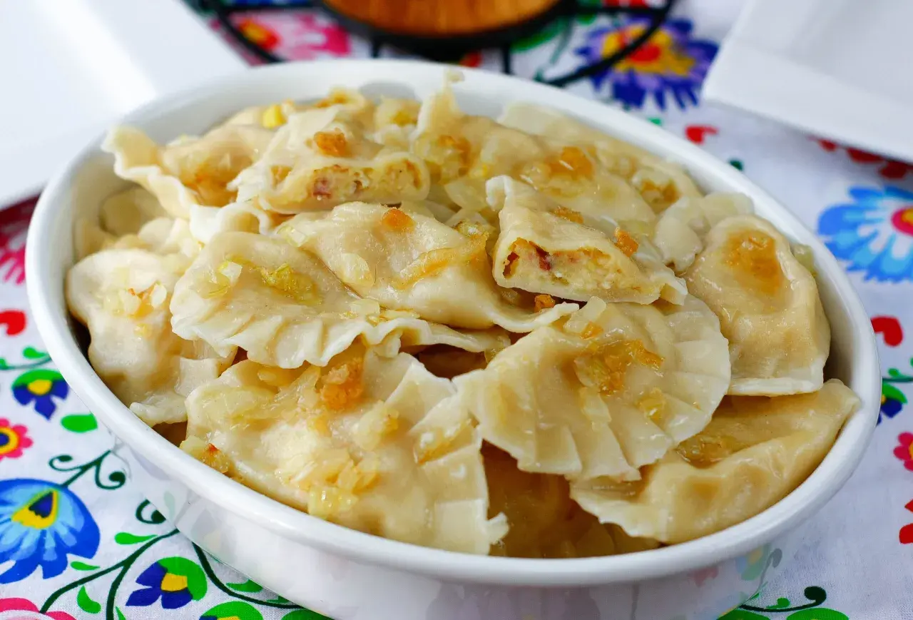 Pyszne pierogi ukraińskie z cebulką i skwarkami, podane w białej misce na kolorowym obrusie.
