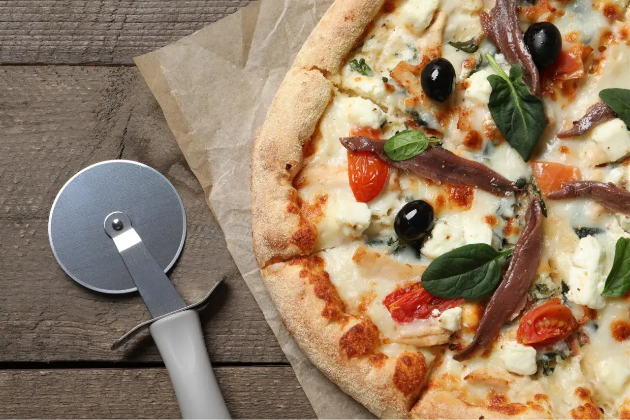 Pyszna pizza margarita z anchois, oliwkami i pomidorkami koktajlowymi, gotowa do pokrojenia.